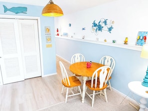 A room with a dining table, chairs, a ceiling light, and wall decorations including a whale and sea turtles. - Little River Inn 1507 (Little River)