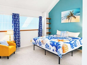 Ein Schlafzimmer mit einem Bett, einem Sessel, einem Fenster mit Vorhängen, einem Bild an der Wand und einem Teppichboden.