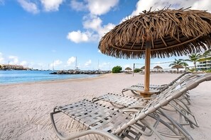 A beach with lounge chairs and a thatched umbrella, a clear sky, and boats in the background. - Amazing Sea Views Condo 3rd Floor with all amenities (Simpson Bay)