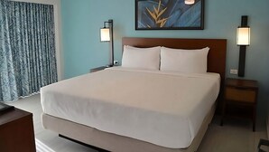 Ein Hotelzimmer mit einem großen Bett, einem Kopfteil, zwei Nachttischen, einem Wandbild und einem Fenster mit Vorhängen.