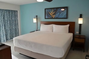 Una camera d'albergo con un letto grande, un comodino con una lampada, un'opera d'arte appesa al muro e una finestra con tende.