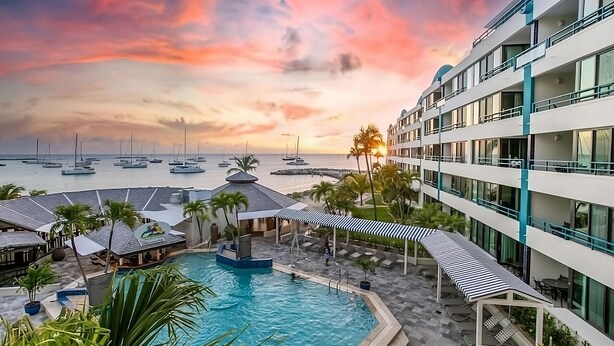 Ein Hotel mit Poolbereich, mehreren Balkonen und Meerblick mit Booten.