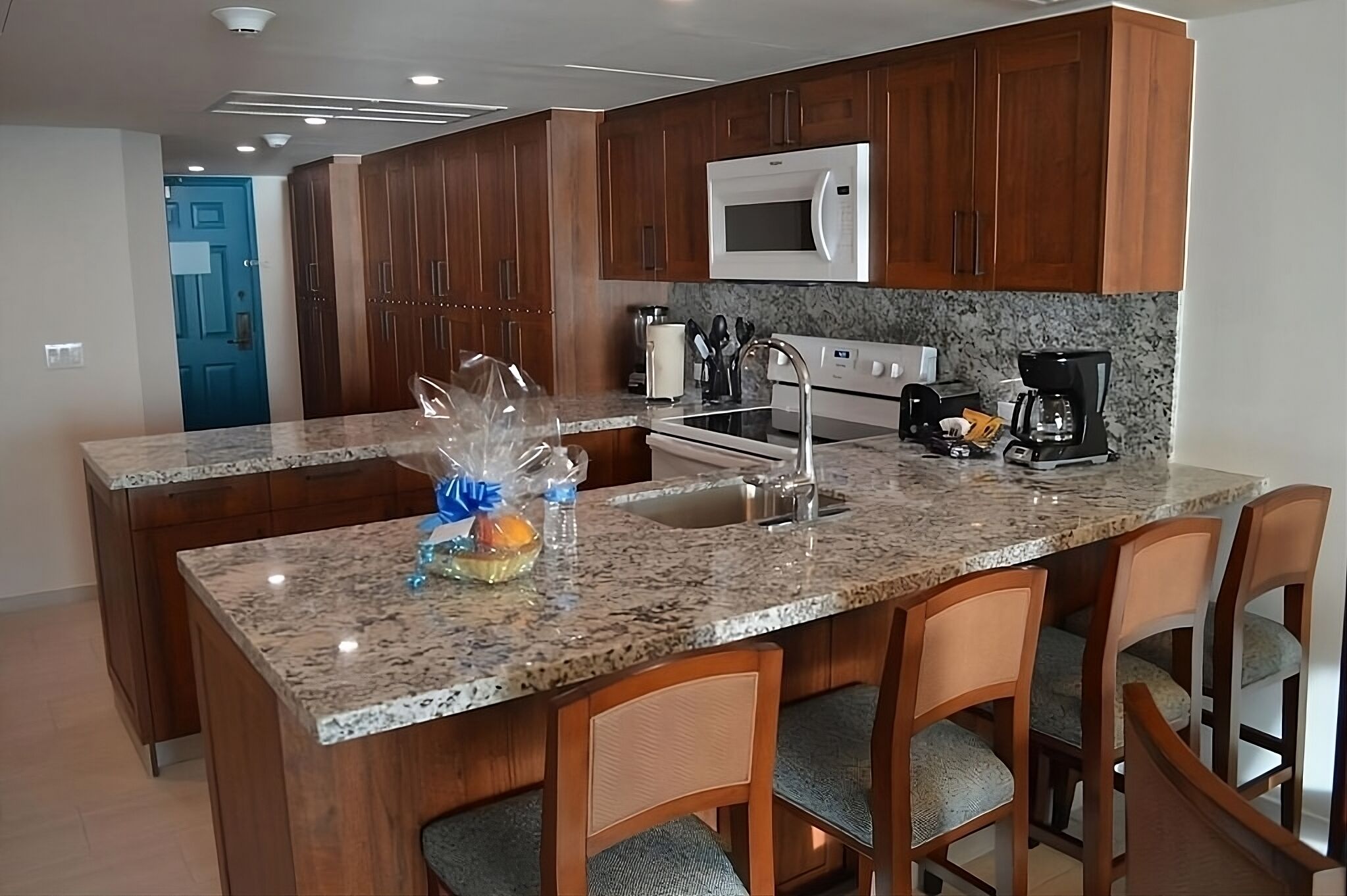 A kitchen with granite countertops, wooden cabinets, a microwave, a stove, and a sink.