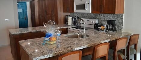 A kitchen with granite countertops, wooden cabinets, a microwave, a stove, and a sink.