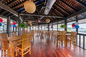 Un'ampia sala da pranzo con tavoli e sedie in legno, ampie finestre e vista sull'acqua.