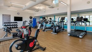 Ein Fitnessstudio mit verschiedenen Trainingsgeräten, darunter Laufbänder und Ergometer, sowie einem an der Wand befestigten Fernseher.