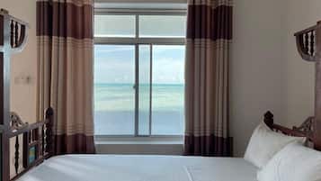 Un dormitorio con una cama grande, cortinas y vista al océano.