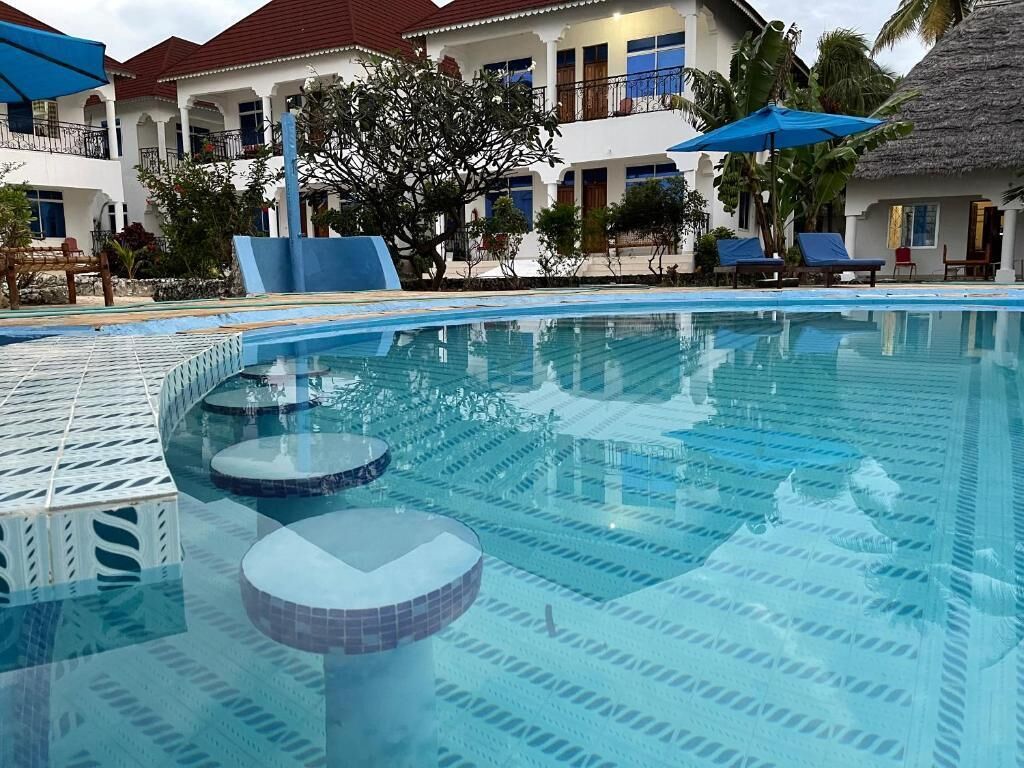 Una piscina con agua cristalina, rodeada de tumbonas y sombrillas, con edificios al fondo.