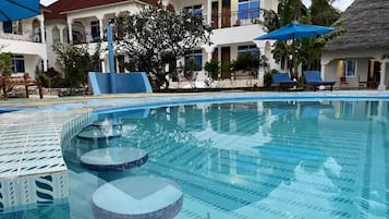 Una piscina con agua cristalina, rodeada de tumbonas y sombrillas, con edificios al fondo.