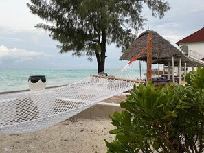 A beach with a hammock, a thatched-roof structure, and a white vase on the sand. - Visitors Inn  (Jambiani)