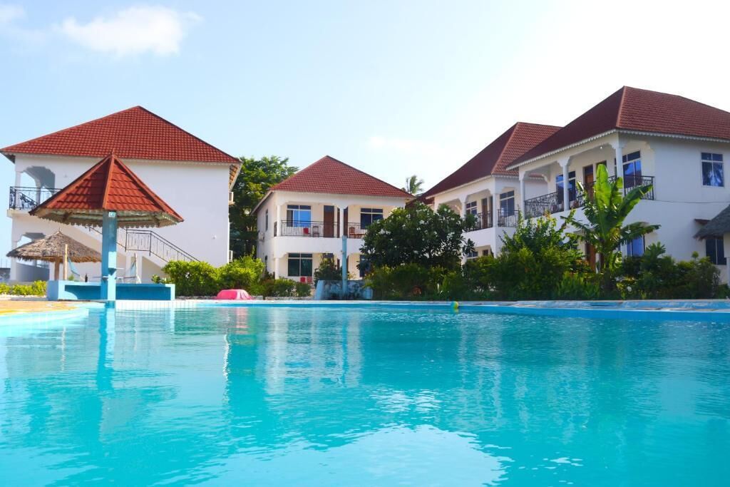 Un hotel con piscina, varias edificaciones con techos rojos y abundante vegetación.
