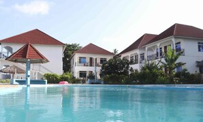 A hotel with a swimming pool, multiple buildings with red roofs, and a covered area. - Visitors Inn  (Jambiani)