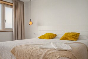 Un lit bien fait, avec une tête de lit blanche et deux oreillers jaunes, une couverture beige et une serviette blanche posée sur le lit.