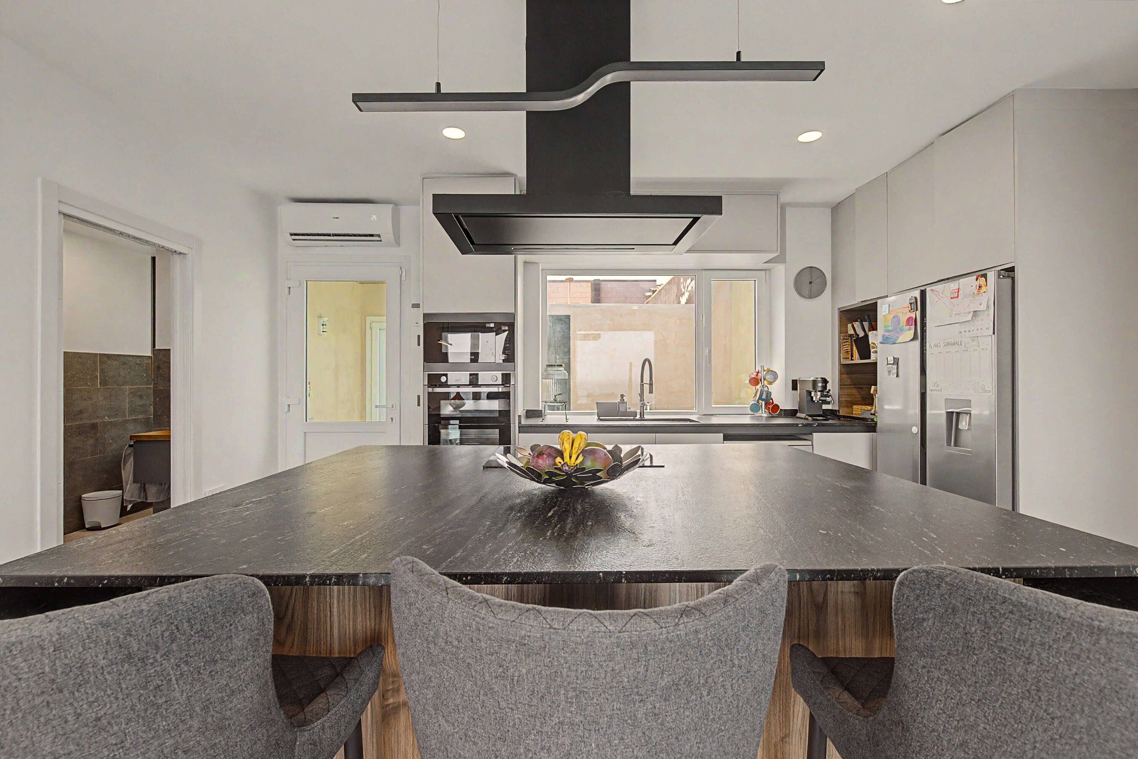 A modern kitchen with a central island, built-in appliances, and a dining area with grey upholstered chairs.