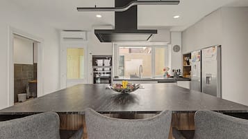 A modern kitchen with a central island, built-in appliances, and a dining area with grey upholstered chairs.