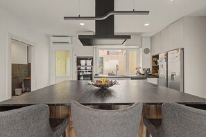 A modern kitchen with a central island, built-in appliances, and a dining area with grey upholstered chairs.