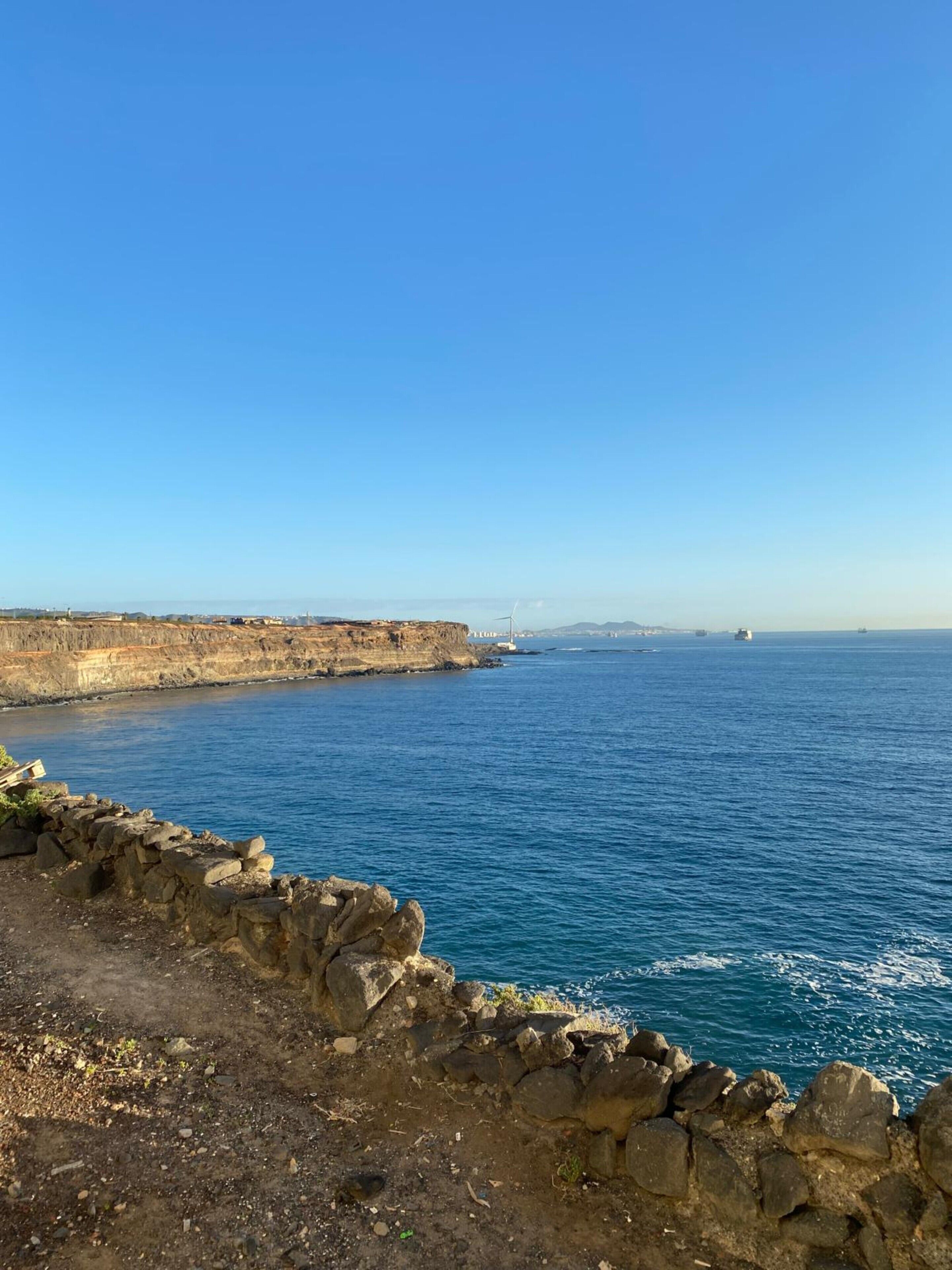 Eine Küstenlandschaft mit blauem Himmel, einer Steinmauer und Blick aufs Meer.