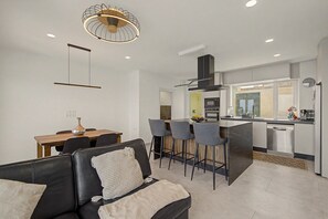 A modern kitchen with a central island, bar stools, and a dining area with a table and chairs.
