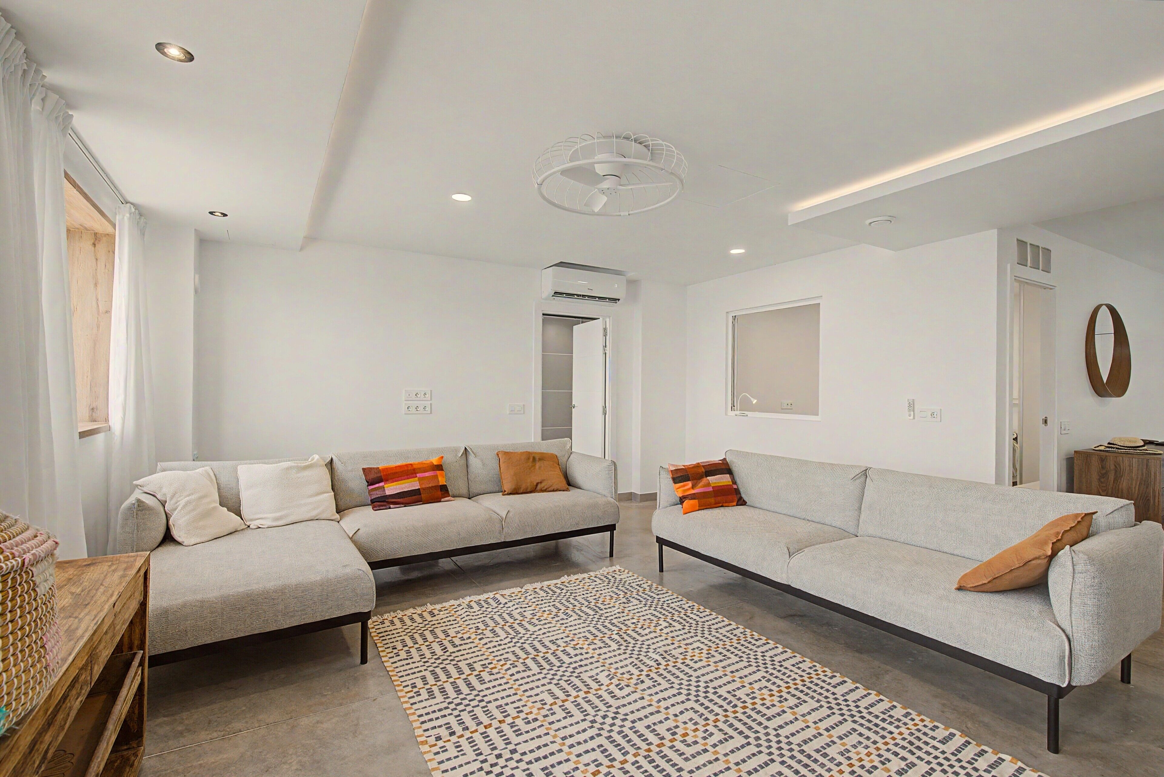 A modern living room with a sofa set, a patterned rug, and a ceiling fan.