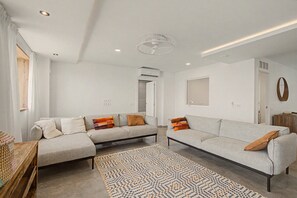 A modern living room with a sofa set, a patterned rug, and a ceiling fan.
