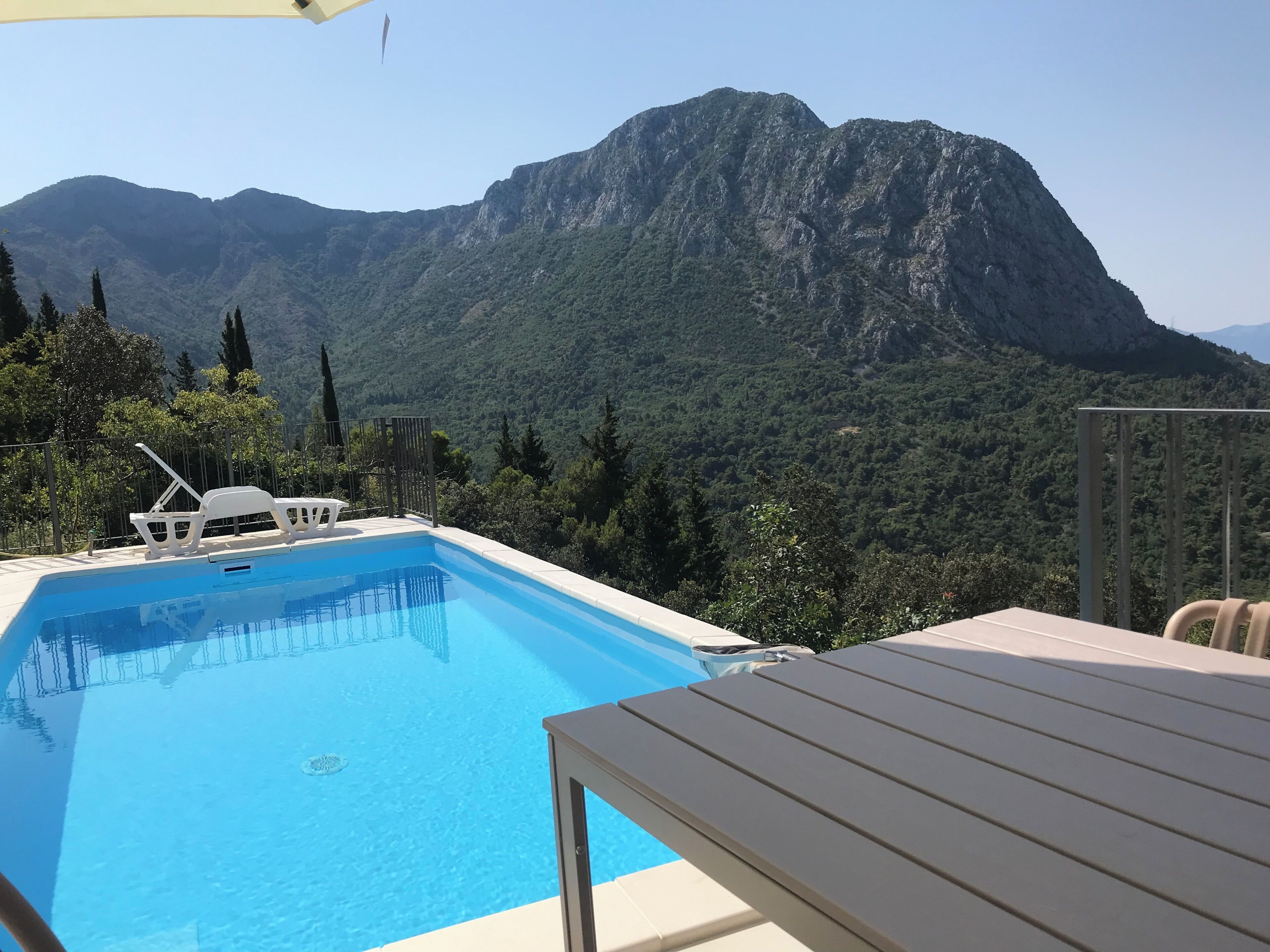 A swimming pool with a mountain view, a lounge chair, and a table.