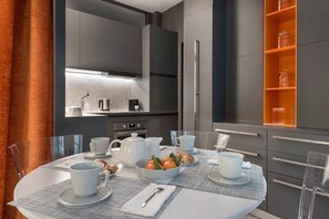 A modern kitchen with grey cabinets, a round dining table with white tableware, and a glass shelf with orange containers. - Grand confort au pied du Louvre (Paris)