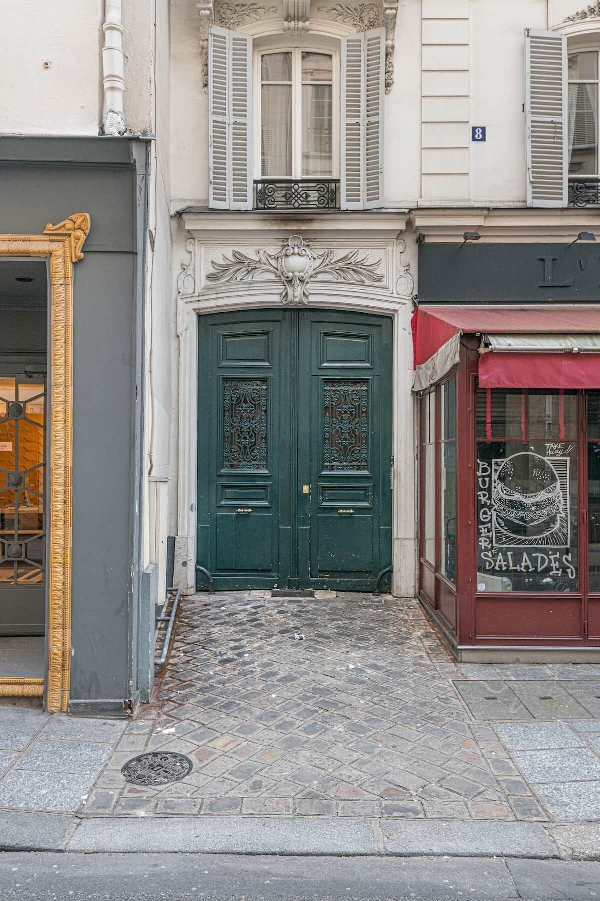 A building with a green double door, a shop with a red awning, and a number '8' sign.