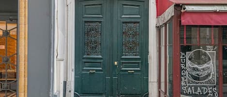 A building with a green double door, a shop with a red awning, and a number '8' sign.