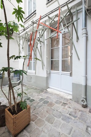 A building with scaffolding, a potted plant, and a stone-paved courtyard. - Grand confort au pied du Louvre (Paris)