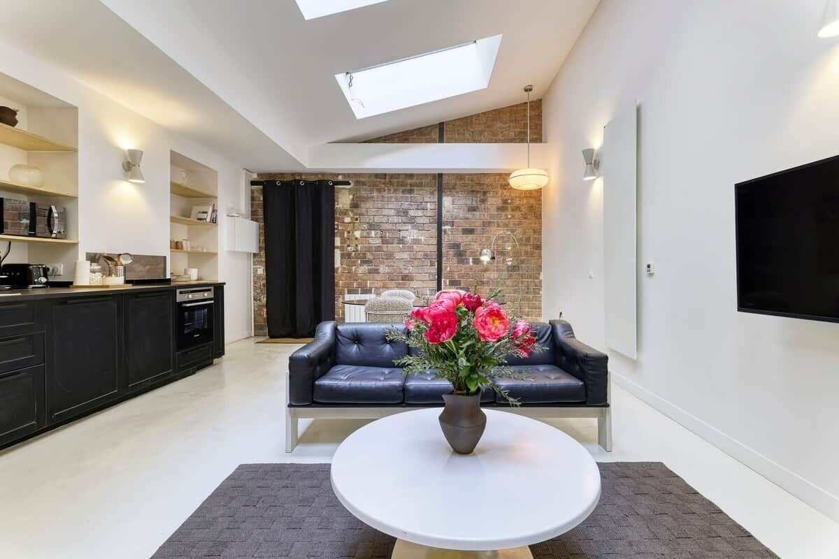 Una sala de estar moderna con un sofá de cuero negro, una mesa de centro redonda blanca y un jarrón con flores.