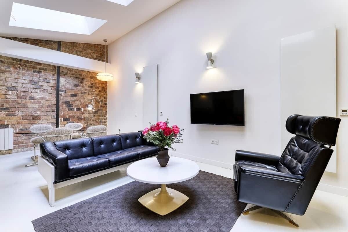 Ein modernes Wohnzimmer mit einem schwarzen Ledersofa, einem schwarzen Ledersessel, einem weißen Couchtisch und einem an der Wand montierten Flachbildfernseher.