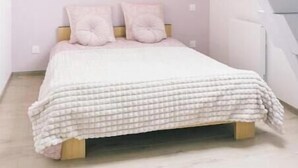 Een slaapkamer met een schuine kap, een bed met een geruit sprei, twee kussens, en een wandlamp.