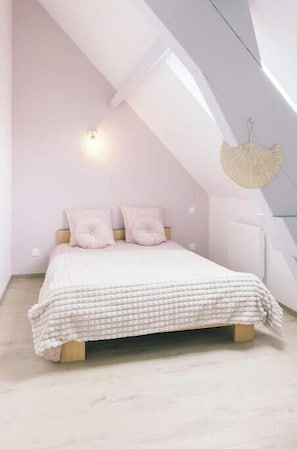 Ein Schlafzimmer mit schrägverdeckter Decke, einem Bett mit kariertem Überwurf, zwei Kissen und einer wandmontierten Lampe.