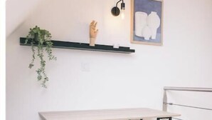 Een kamer met een bureau, een stoel, een plank met een plant, een wandlamp en een ingelijste foto.