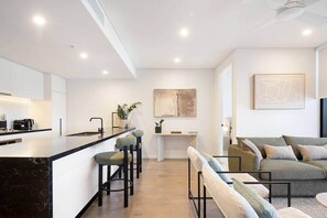 Eine moderne Küche mit Kochinsel, Barhocker, Essbereich und einem Wohnzimmer mit Sofa und Couchtisch.