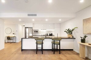 Uma cozinha moderna com uma ilha central, banquetas, micro-ondas e geladeira.