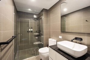 Ein modernes Badezimmer mit einer gläsernen Dusche, einer weißen Toilette, einem weißen Waschbecken mit schwarzer Arbeitsplatte und einem großen Spiegel.