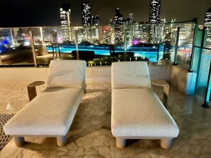 Two lounge chairs with cushions, a small table, and a cityscape view at night. - Luxury 2BR Apt, Pool, Parking, Skye Kangaroo Pt (Kangaroo Point)