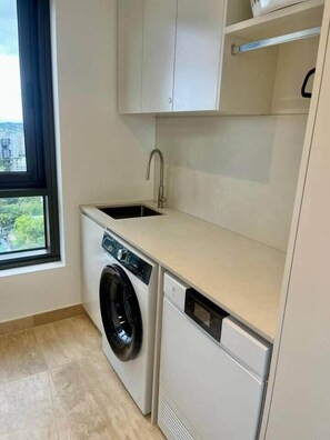 A compact laundry room with a washing machine, a dishwasher, and a sink. - Luxury 2BR Apt, Pool, Parking, Skye Kangaroo Pt (Kangaroo Point)