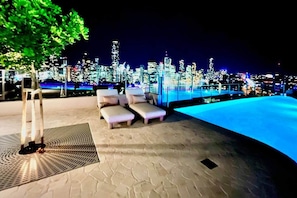 A nighttime cityscape with a pool area featuring lounge chairs and a tree. - Luxury 2BR Apt, Pool, Parking, Skye Kangaroo Pt (Kangaroo Point)