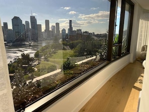 Een kamer met een groot raam dat uitkijkt over een stadsbeeld en een park.