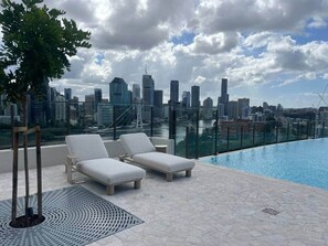 A rooftop pool area with lounge chairs and a city skyline view. - Luxury 2BR Apt, Pool, Parking, Skye Kangaroo Pt (Kangaroo Point)