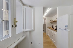 Ein schmaler Flur mit einer Küchenzeile, die weiße Schränke, einen Kühlschrank und eine Mikrowelle umfasst.