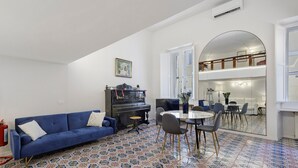A living room with a blue sofa, a piano, and a dining area with a round table and chairs. - Apartment 'Navona Haven' with Wi-Fi and Air Conditioning (Rome)