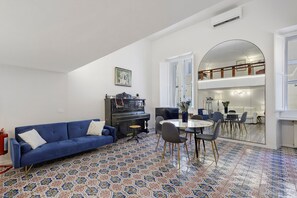 A living room with a blue sofa, a piano, and a dining area with a round table and chairs. - Apartment 'Navona Haven' with Wi-Fi and Air Conditioning (Rome)