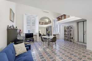 Un salón con sofá azul, televisor, piano y comedor con sillas y mesa.