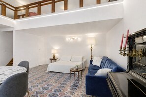 A hotel room with a bed, a blue sofa, a small table, a lamp, and a decorative candelabra. - Apartment 'Navona Haven' with Wi-Fi and Air Conditioning (Rome)