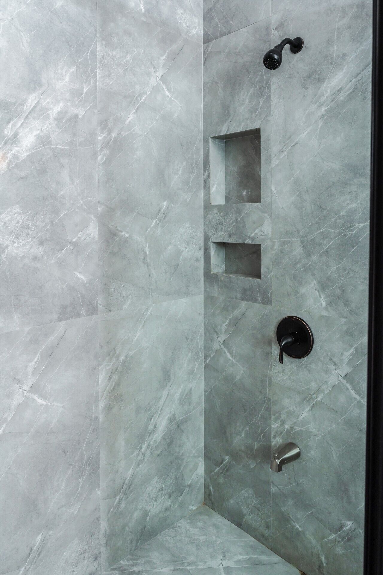 Une douche avec un mur en marbre, un pommeau de douche à main, un robinet mural et un distributeur de savon.