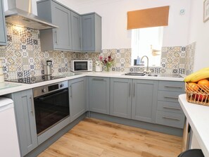A modern kitchen with grey cabinets, a microwave, an oven, and a sink. - The Old Post Office (Ventnor)