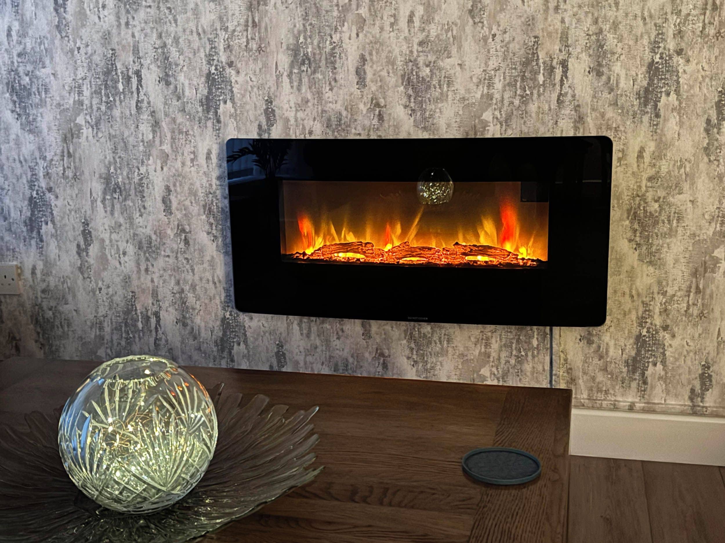 Un caminetto dal design moderno, un oggetto di vetro decorativo su un tavolo di legno e una parete strutturata sullo sfondo.
